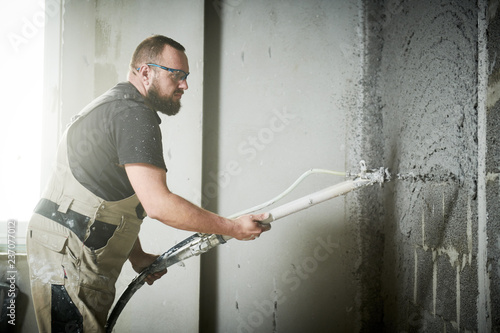 Plasterer using screeder spraying putty plaster mortar on wall photo