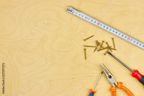 screwdriver and pliers with screws lie on the plywood. copy space. DIY concept.