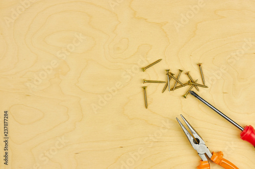 screwdriver and pliers with screws lie on the plywood. copy space. DIY concept.