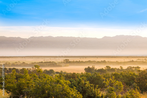 Croatia, Dalmatia, Velebit mountain ridge and misty fields in foreground, summer morning