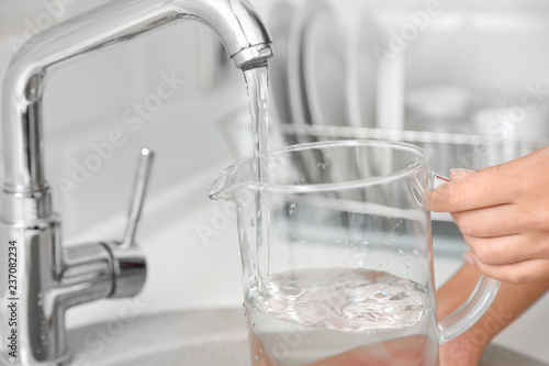 Woman pouring water into glass jug in kitchen, closeup