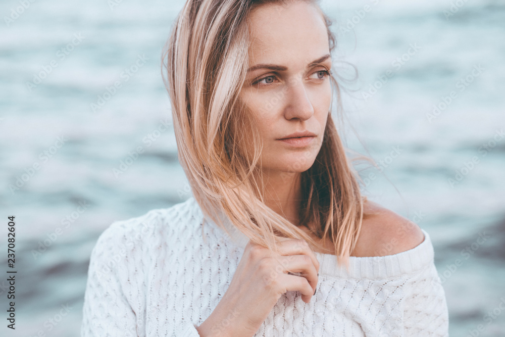 Beautiful young girl in a white sweater walking alone the beach. Perfect hair and skin. Outdoor shot. Beautiful young girl in a white sweater walking alone the beach. Perfect hair and skin. Outdoor shot.