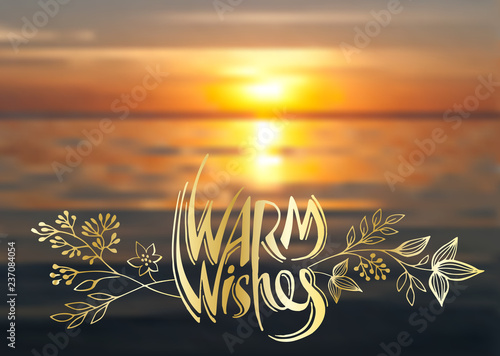 Warm wishes, vector lettering, handwritten golden text and floral elements on blurred background of sea sunset photo