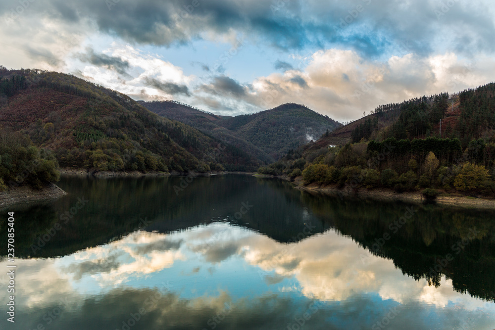 Nubes y montañas reflejadas en un embalse