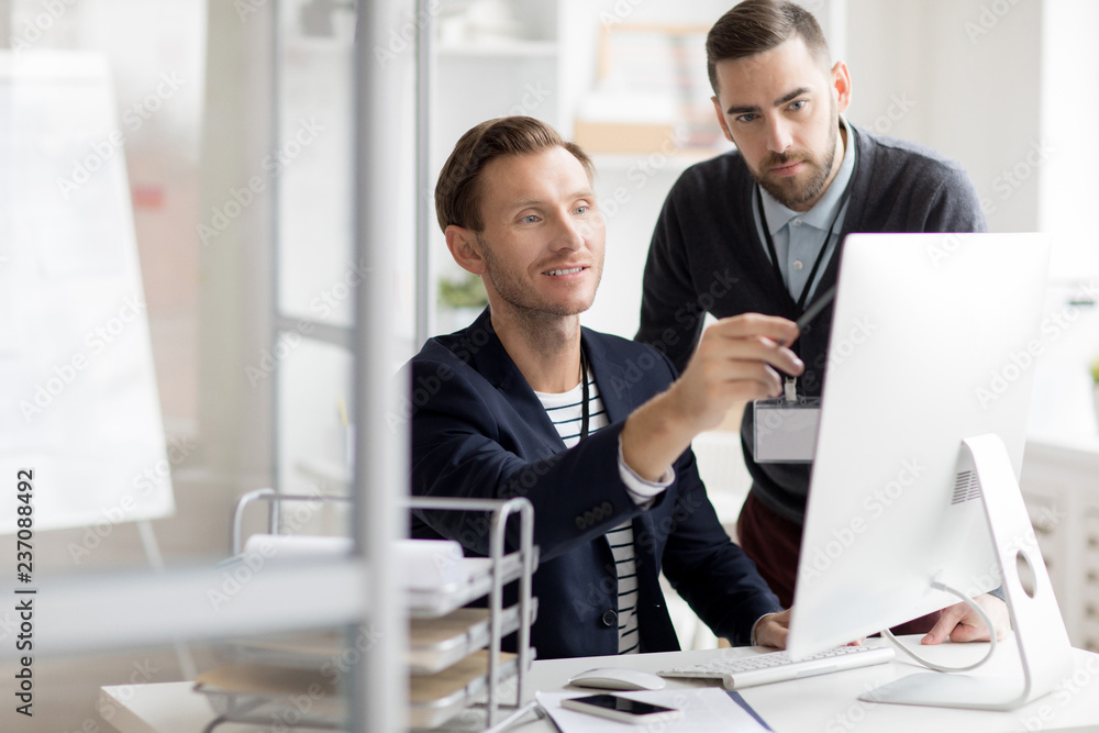 Portrait of two professionals looking at computer screen while working in modern office, copy space Portrait of two professionals looking at computer screen while working in modern office, copy space