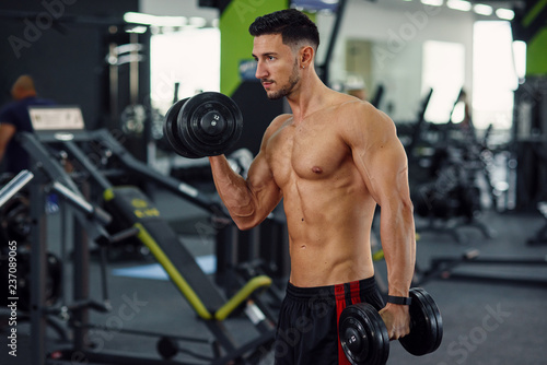 Close up of sporty fitness man doing exercises for biceps using dumbbells on the stylish gym background.