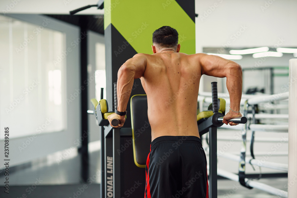 Strong healthy man doing push-ups on parallel bars while training in modern gym. Back view. Sporty and healthy concept. Strong healthy man doing push-ups on parallel bars while training in modern gym. Back view. Sporty and healthy concept.