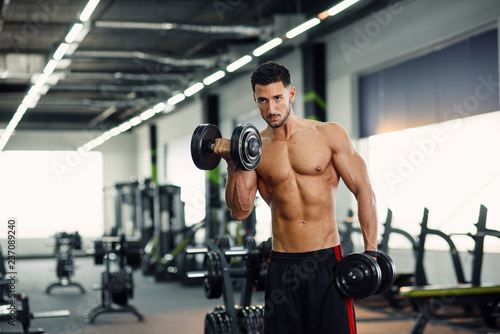Strong healthy man doing biceps exercises with dumbbells on the training in modern gym.