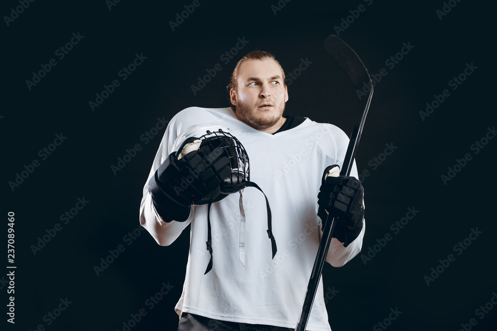 Obraz premium Frightened hockey player in protective white uniform holding white hard hat and hockey stick looking aside with anxious or alarmed expression, isolated over black background