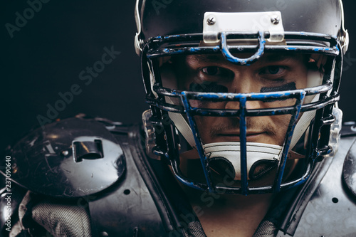 Face portrait of manly loooking young sportsman in black protective headgear and armour, looking courageously at camera, determined to win