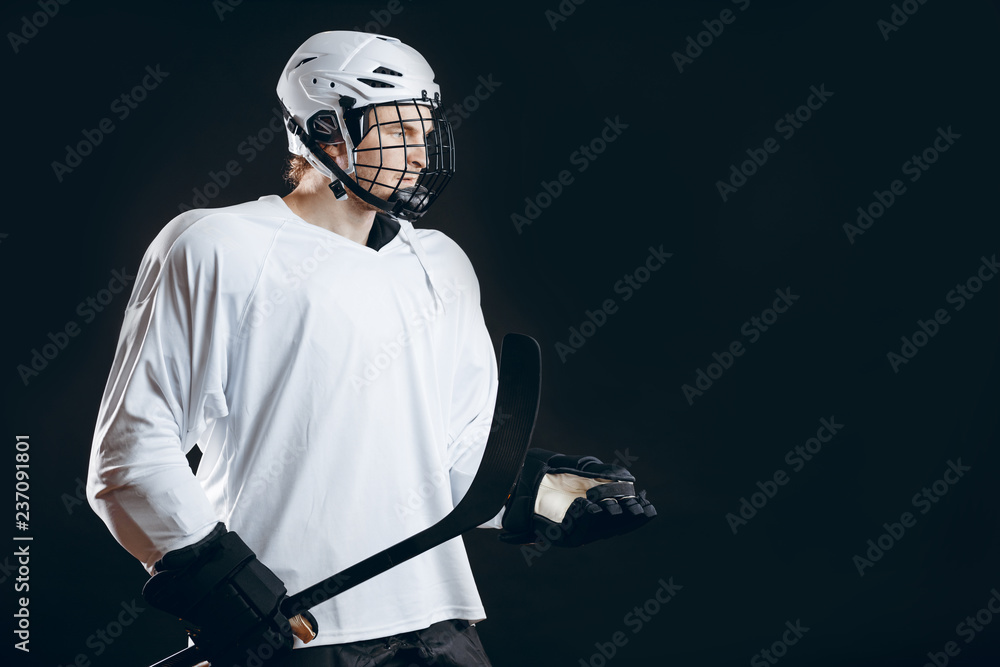 Hockey team trainer in white uniform and protective headgear on head. throws a puck in the air, holding hockey stick over the black background with copyspace.