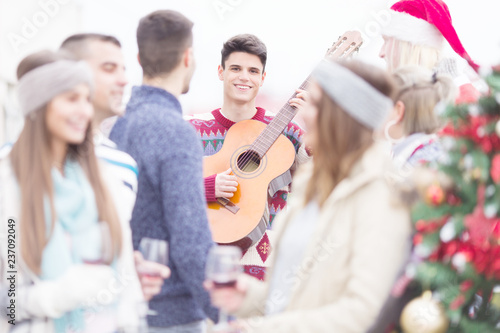 Young man with guitar smiling and celebrating Christmas on balcony with friends