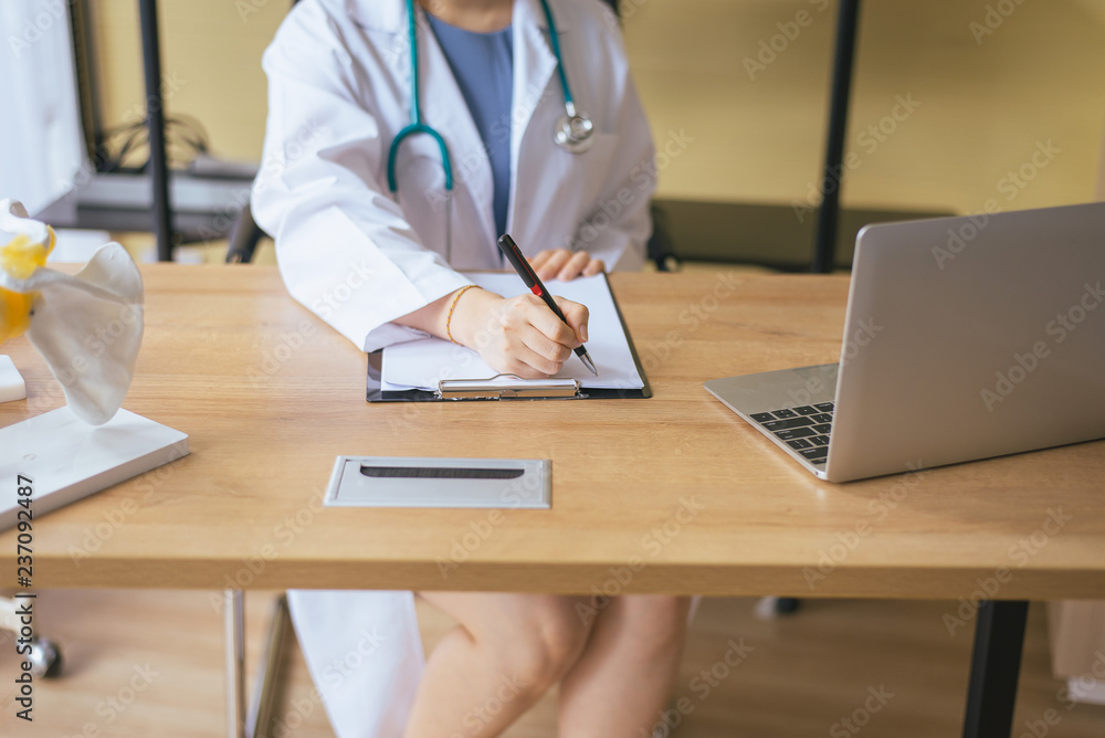 Close up of hands doctor woman writing note with pen on table at hospital Close up of hands doctor woman writing note with pen on table at hospital
