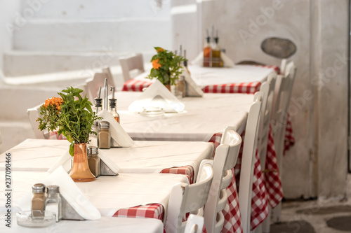 Fototapeta Naklejka Na Ścianę i Meble -  Perspective view of tables in a line outdoors in a Greek taverna in Mykonos, Greece.