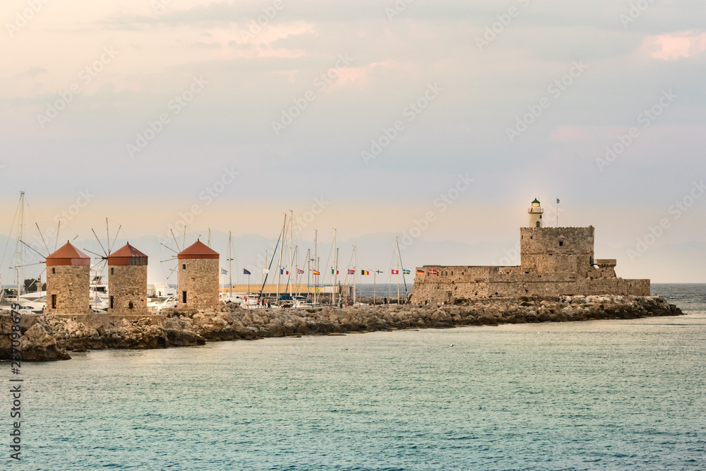 Windmills and the lighthouse at Mandraki Harbour, Rhodes, Greece.
