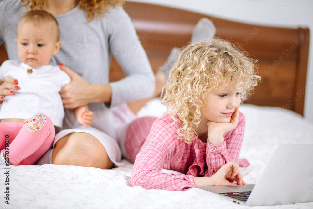 beautiful girl with curly hair watching cartoons while her mother is sitting with a baby indoors. close up cropped photo. beautiful girl with curly hair watching cartoons while her mother is sitting with a baby indoors. close up cropped photo.