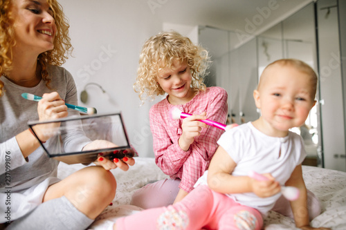 cheerful red-haired woman and her daughter tickling the baby with brushes indoors. close up photo