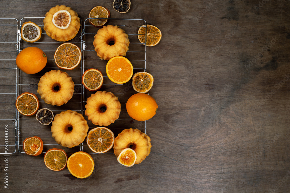 Small orange Bundt cakes with fresh and dry oranges on cooling ruck, top view, flat lay, copy space Small orange Bundt cakes with fresh and dry oranges on cooling ruck, top view, flat lay, copy space