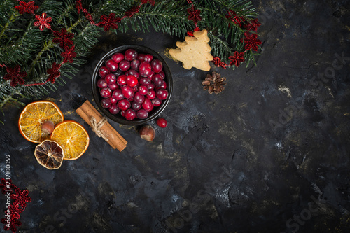 Christmas background with Christmas tree branch, dry oranges, sticks of cinnamon and bowl of fresh cranberries, top view