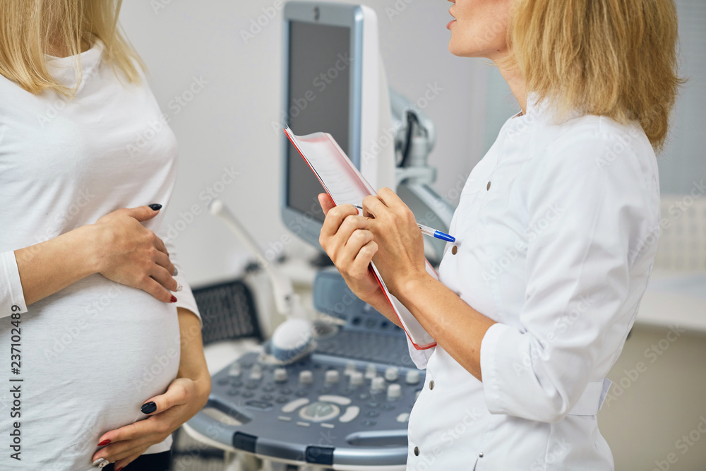doctor writing down the complaints of a female pregnant client. client's care. close up side view photo doctor writing down the complaints of a female pregnant client. client's care. close up side view photo