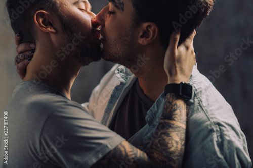 Mixed race couple of Gay Male Sexual Interactions, close up. Asian and Caucasian men cuddling and kissing each other against grey loft background