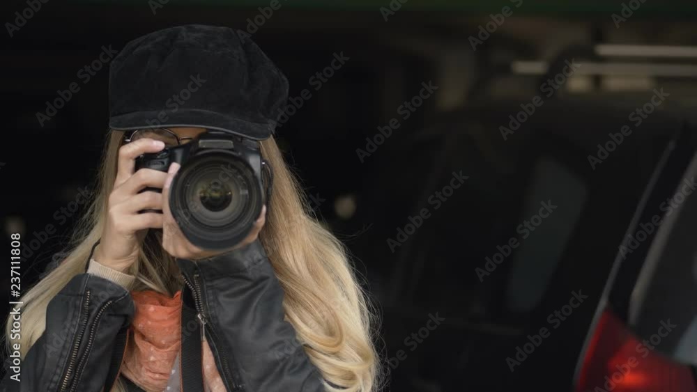 Professional young blonde woman photographer with digital camera taking pictures at city parking. Close Up, shallow depth of field, dark background. Professional young blonde woman photographer with digital camera taking pictures at city parking. Close Up, shallow depth of field, dark background.