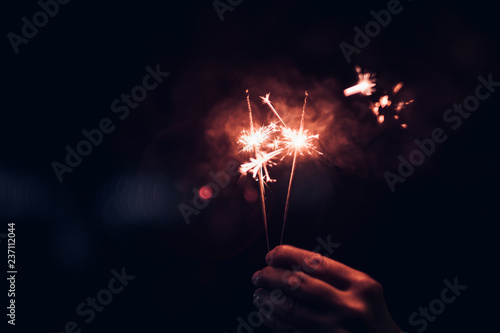 Hand holding burning Sparkler blast on a black bokeh background at night,holiday celebration event party,dark vintage tone.