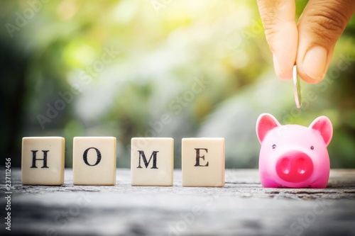 Business concept, hand putting coins in pink piggy bank for home photo