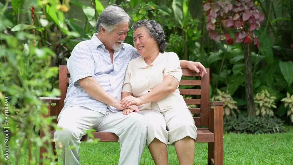 Senior couple sitting and talking together in home garden. Retired old Asian male and female, holding hands, happy smile. Senior lifestyle concept. Senior couple sitting and talking together in home garden. Retired old Asian male and female, holding hands, happy smile. Senior lifestyle concept.