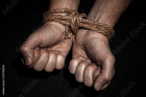 Man with hands tied with rope on black background. The concept of slavery or prisoner. photo
