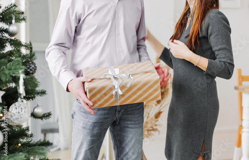 The man holding gift box for woman his wife on the background of Christmas tree