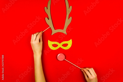 Fototapeta Naklejka Na Ścianę i Meble -  Woman's hand making flat designed funny decorating santa's christmas deer with horns and red nose with comic glasses eyes isolated on red background. Merry Christmas and Happy New Year concept.