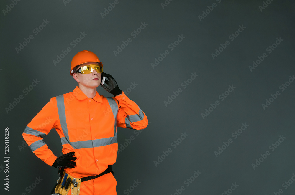 Builder worker in a hardhat is talking on a mobile phone and is looking up isolated on gray background with copy space. Builder worker in a hardhat is talking on a mobile phone and is looking up isolated on gray background with copy space.