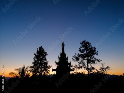 Buddhist pagoda silhouette with trees at sunset © Cyrsiam