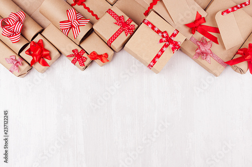 Christmas gifts background - various craft paper gifts with red ribbons and bows, blank label on soft light white wood board, flat lay. © finepoints