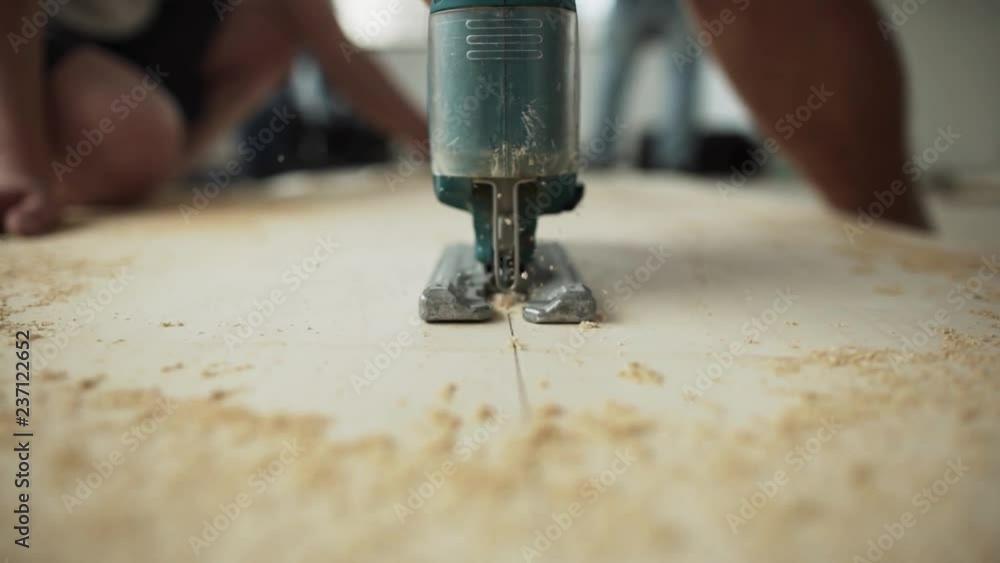 Camera shows working process of green dusty electric jigsaw operated by man's hand and cutting wooden plank according drawn line on its surface somewhere in workhouse. Camera shows working process of green dusty electric jigsaw operated by man's hand and cutting wooden plank according drawn line on its surface somewhere in workhouse.