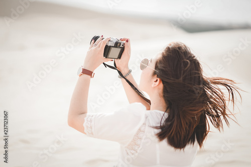 Traveling and photography. Young woman with camera taking photo at White Sand Dunes, Vietnam.
