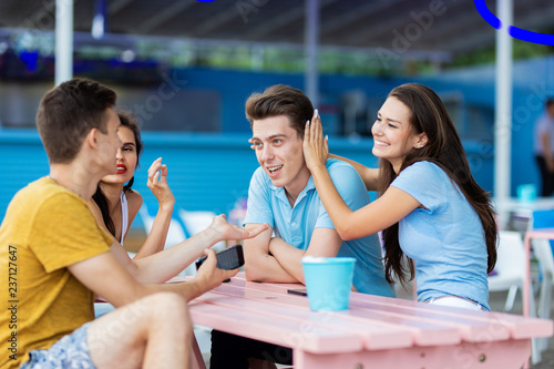 A company of good-looking friends is laughing and sitting at the table in the nice summer cafe. Entertainment, having good time. Friendship.