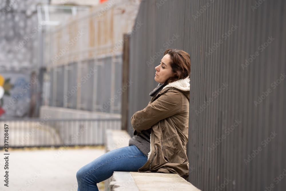 Depressed young woman sitting on urban city street overwhelmed a