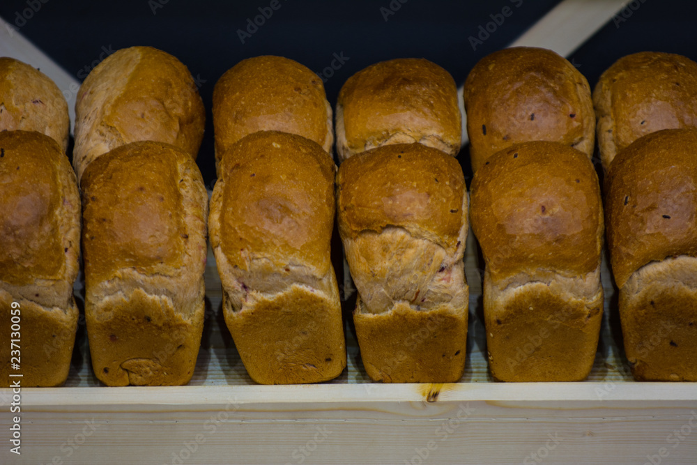 Many breads in the bakery stand on wooden shelves. Fresh flavored loaves