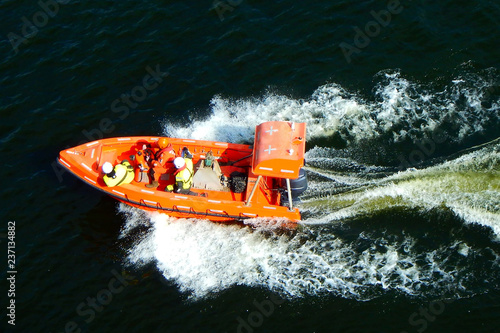 Bild auf Leinwand People in lifeguard jackets in orange rescue safe boat with sea around