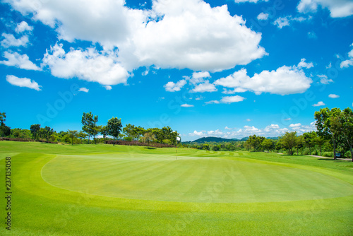 Green grass in golf course with mountain and blue cloud sky background