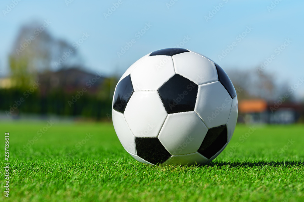Classic soccer ball lying on the bright green grass on the football field in the background of the stands for the fans at the sports stadium close-up in a large sports center for football players