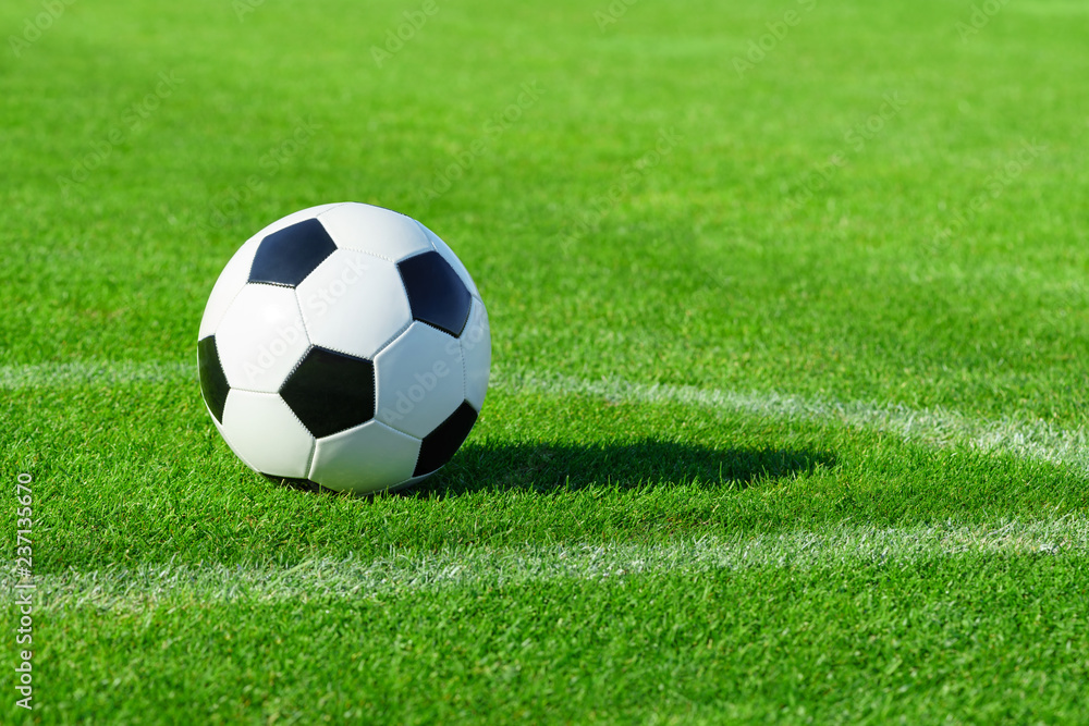 A classic soccer ball lies on the bright green grass on the football field in the designated area of the penalty area at a sports stadium close-up in a large sports center for football players