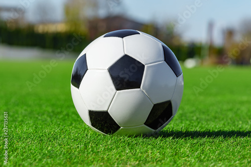 Classic soccer ball lying on the bright green grass on the football field in the background of the stands for the fans at the sports stadium close-up in a large sports center for football players