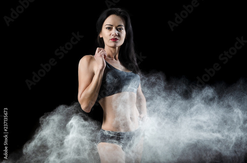 Graceful woman posing in a cloud of dust on a black background