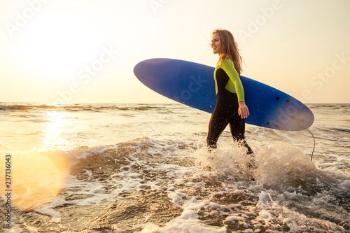 Photography Young freelancing woman in a wetsuit swimming over surfboard in the water at beach
