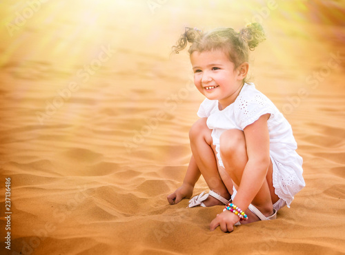 Little girl smiles and plays sand in the desert. photo