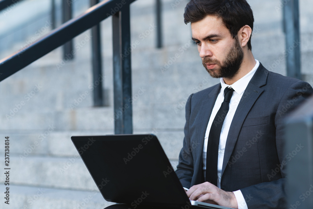 Businessman in a suit sitting on the steps and working on a laptop. Businessman in a suit sitting on the steps and working on a laptop.