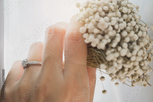 Close up of an elegant diamond ring on woman finger while holding white flower. soft and selective focus.Love and wedding concept.